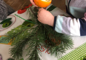 Dzieci układają kompozycję z pomarańczy na gałązce choinki