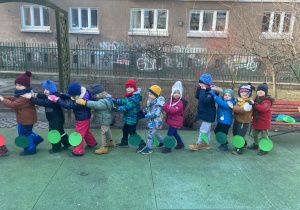 Dzieci stworzyły długą gąsienicę i wędrują po ogrodzie przedszkolnym