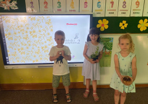 Dzieci prezentują sadzonkę mięty, nasionka i domek dla pszczół