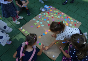 Dzieci na tarasie wykonują wspólny kolaż przyklejając kolorowe papierowe kółka