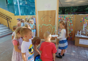Dzieci podczas smarowania klejem sylwety żaby i przyklejania zielonych pianek