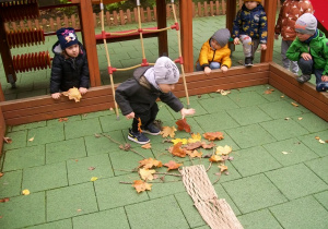 Chłopiec układa liście na gałązkach drzewa tworząc w ten sposób koronę