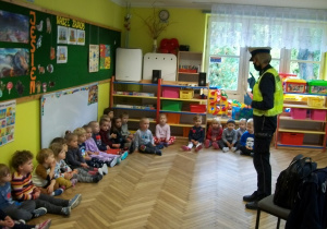 Pani policjantka pokazuje dzieciom jak należy się ubrać, aby być lepiej widocznym na ulicy.